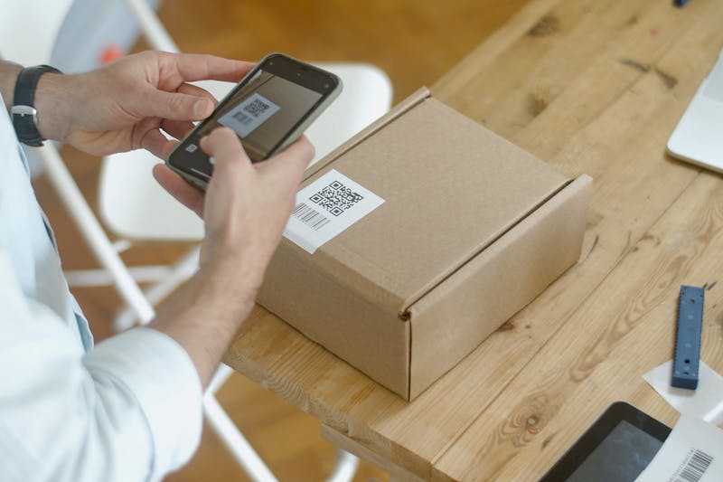 Person scannt einen QR-Code auf einem Paket mit dem Smartphone